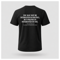 Male model wearing a black Politics Is Interested In You T-shirt with the Marshall Berman political quote printed in distressed white text across the back.