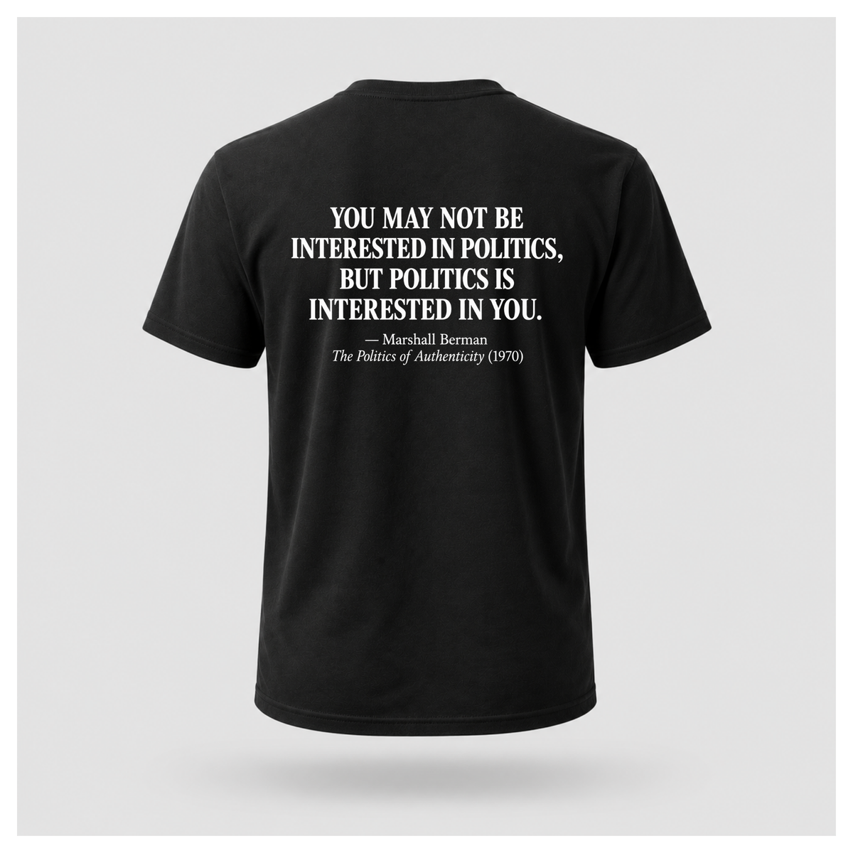 Male model wearing a black Politics Is Interested In You T-shirt with the Marshall Berman political quote printed in distressed white text across the back.