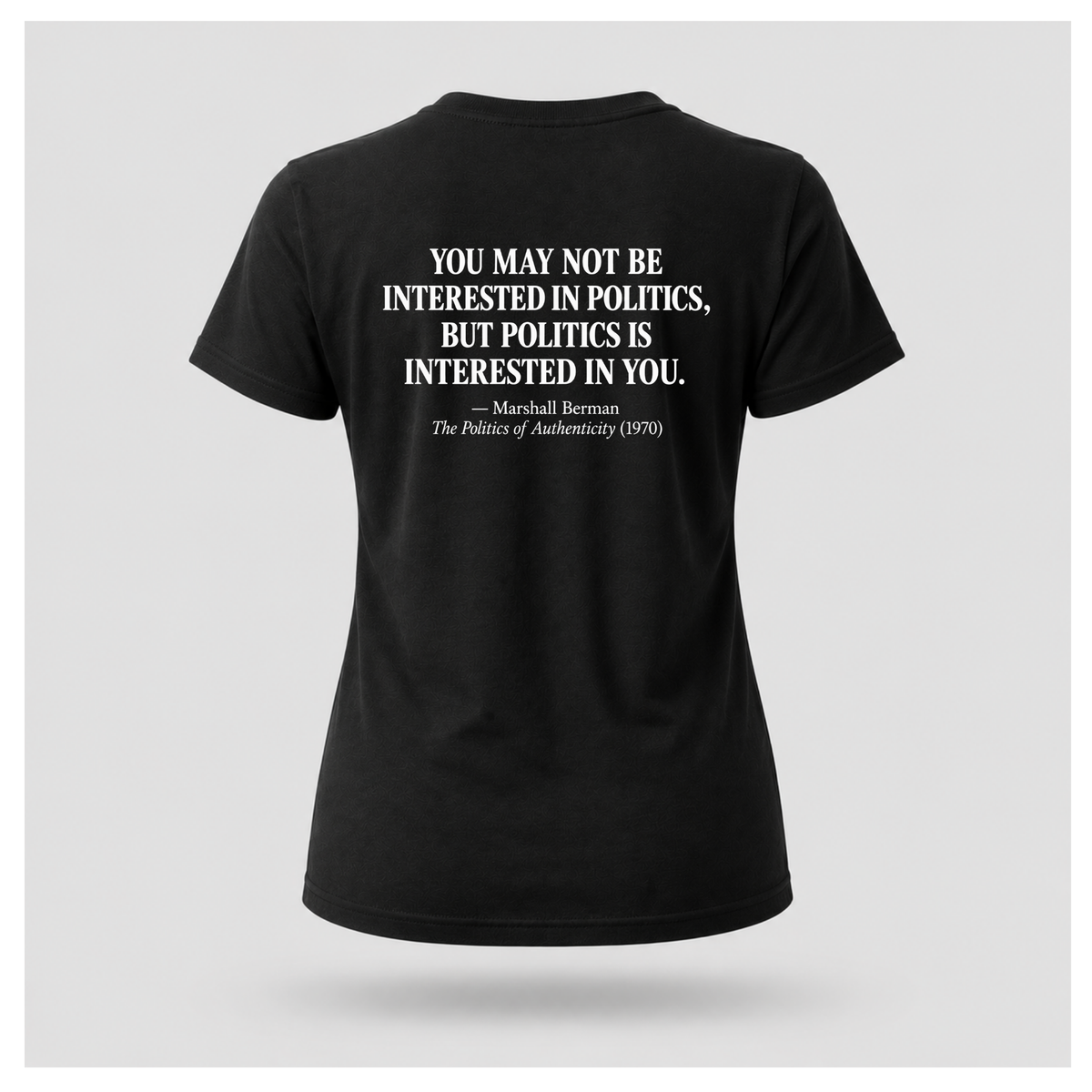Female model wearing a black Politics Is Interested In You T-shirt with the Marshall Berman political quote printed in distressed white text across the back.