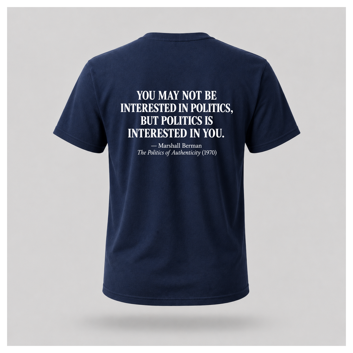 Male model wearing a navy blue Politics Is Interested In You T-shirt, showing the distressed white Marshall Berman quote on the back.