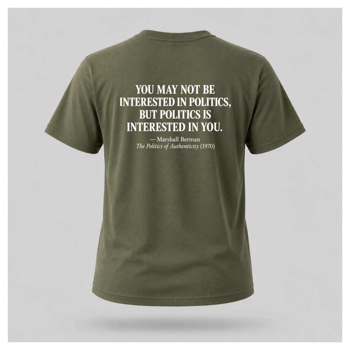 Male model wearing a military green Politics Is Interested In You T-shirt with the distressed white Marshall Berman quote printed on the back.
