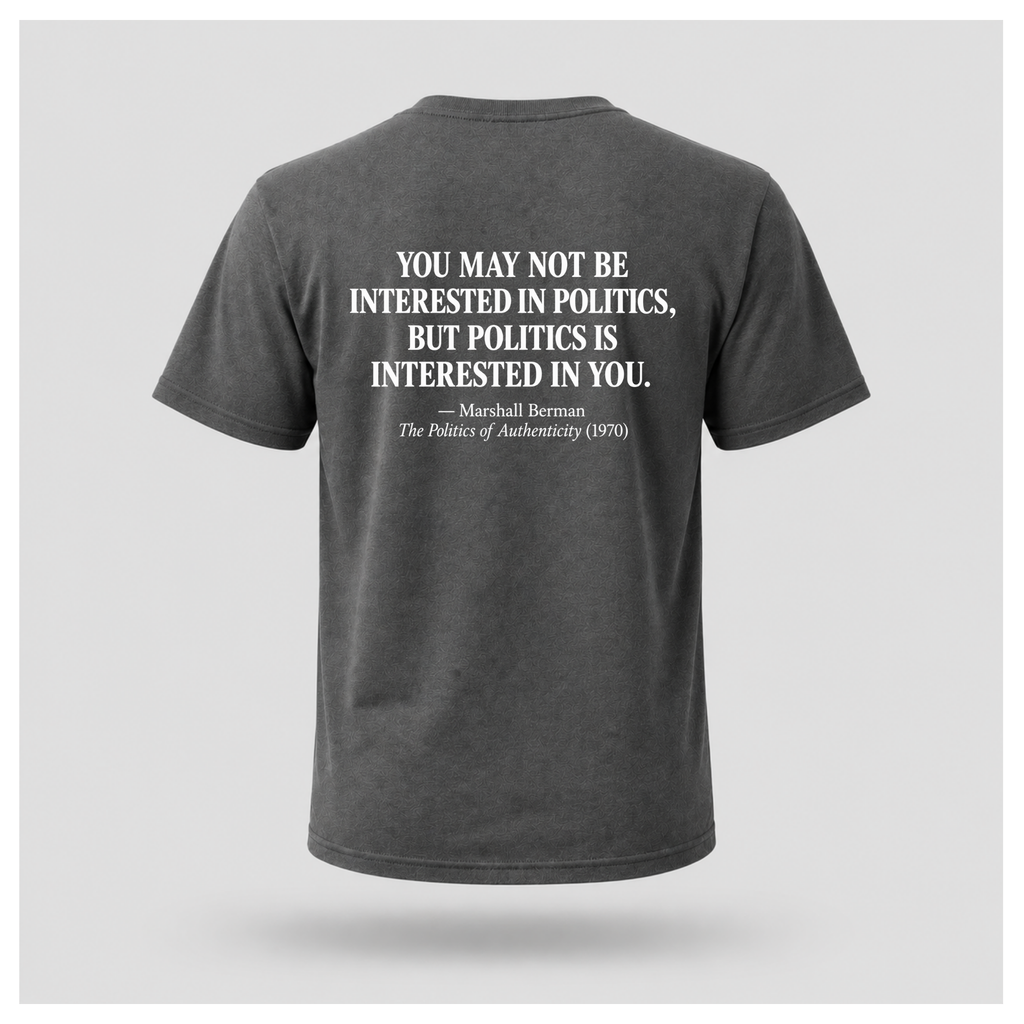 Male model wearing a charcoal grey Politics Is Interested In You T-shirt with the distressed white Marshall Berman quote printed on the back.