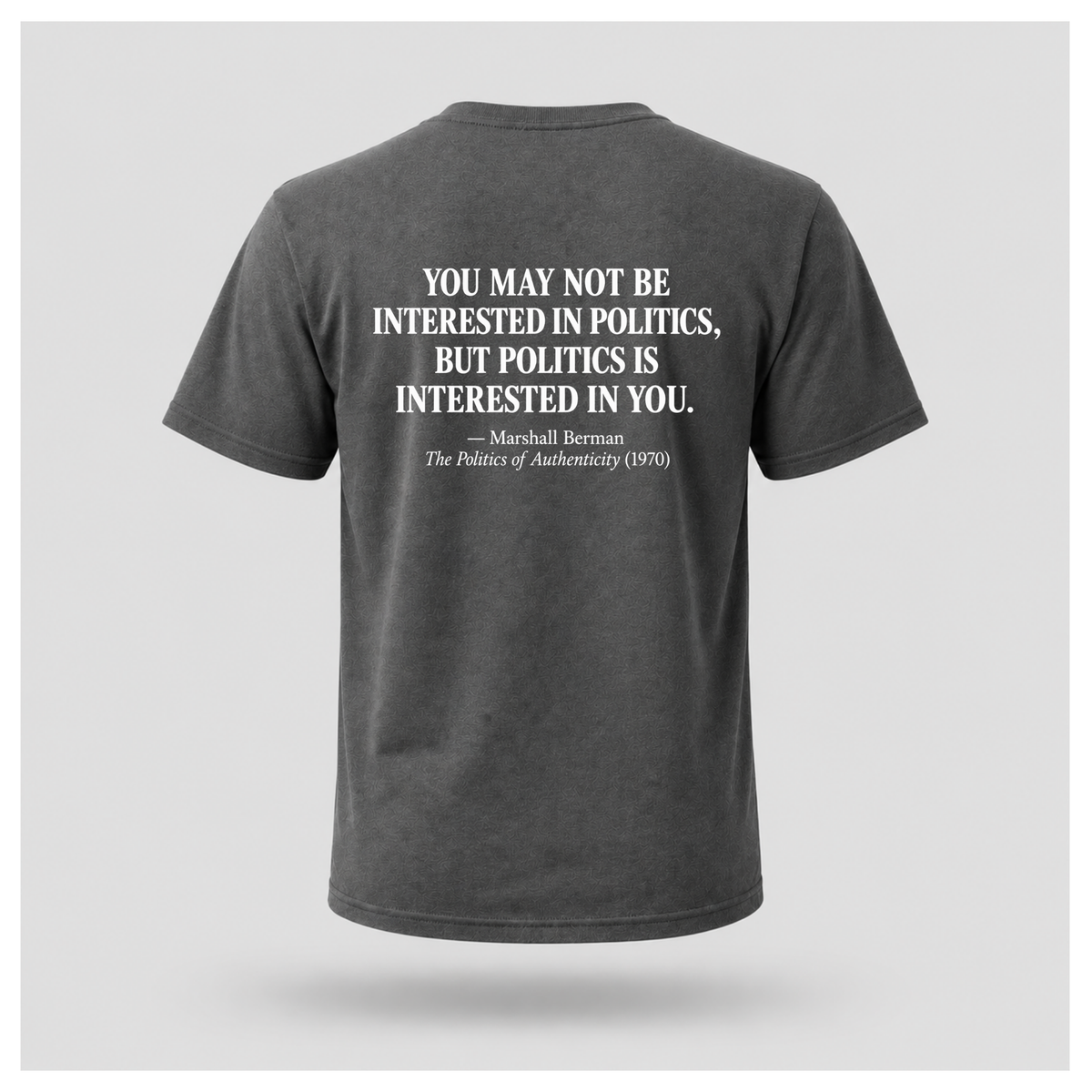Male model wearing a charcoal grey Politics Is Interested In You T-shirt with the distressed white Marshall Berman quote printed on the back.