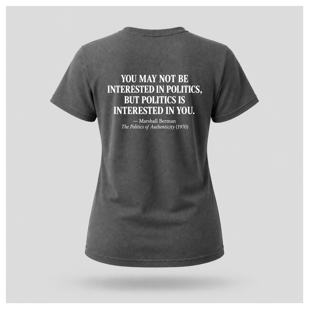 Female model wearing a charcoal grey Politics Is Interested In You T-shirt with the distressed white Marshall Berman quote printed on the back.