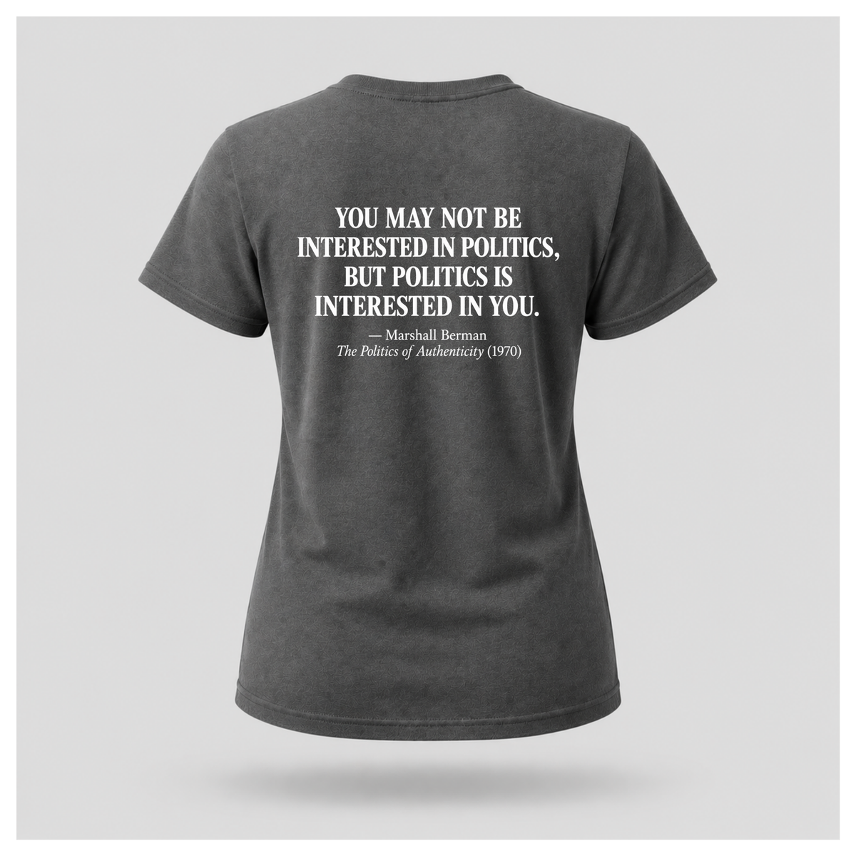 Female model wearing a charcoal grey Politics Is Interested In You T-shirt with the distressed white Marshall Berman quote printed on the back.